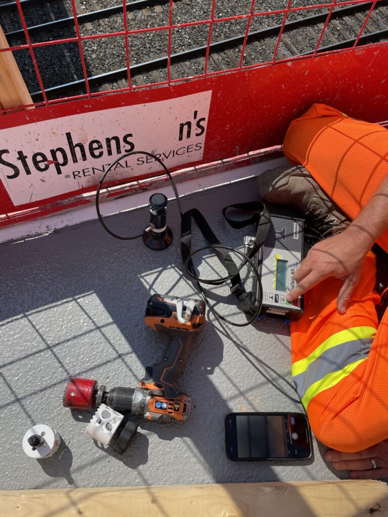 coating inspector in Toronto performing a coating adhesion test with inspection tools and drill on a job site near railway tracks